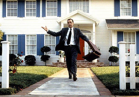 Photo of Kevin Spacey walking out of a suburban home with a white fence in 'American Beauty'