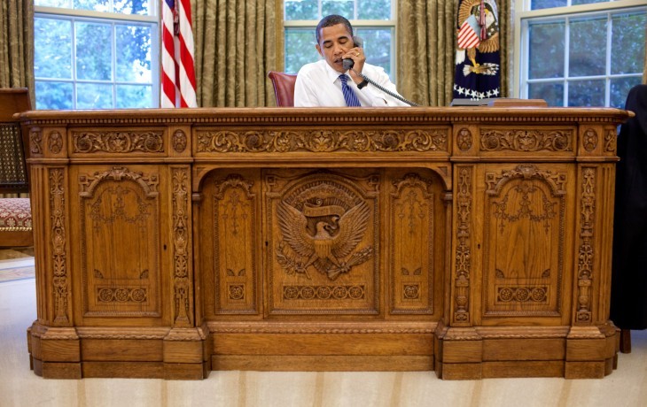 Barack Obama sits behind the heavy and ornate wood Resolute desk
