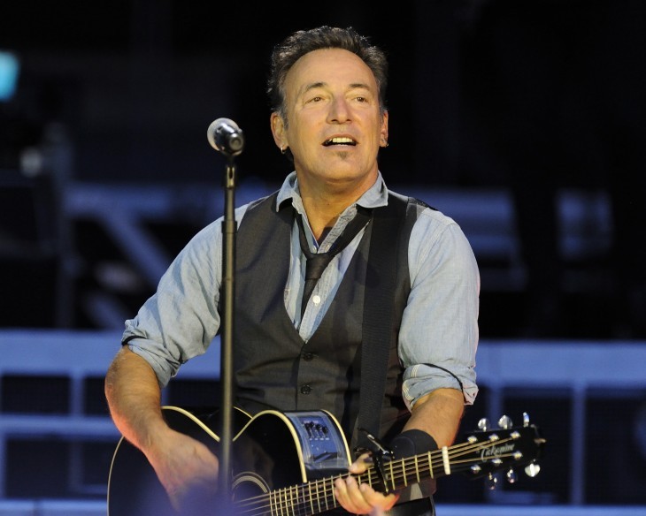 Photo of Bruce Springsteen with guitar and vest onstage in 2012