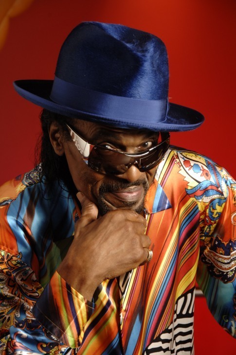 A photo of Chuck Brown in a riotous rainbow shirt with shades and a smart blue fedora, smiling