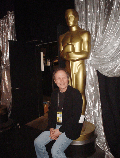 Billy Crystal sits in front of a huge gold Oscar statuette