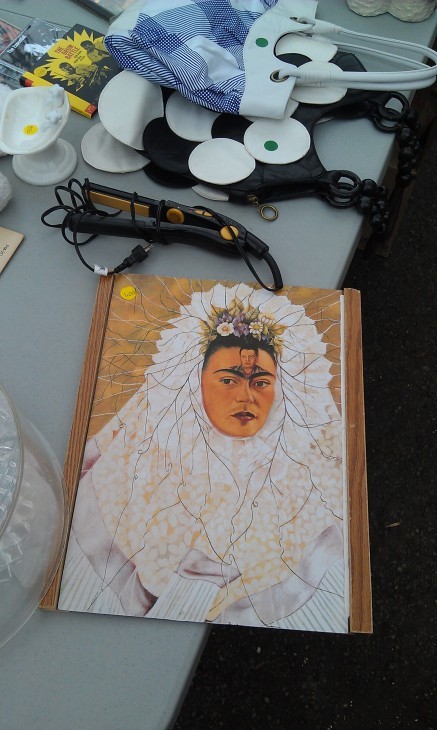 A photo of a self-portrait of Frida Kahlo in a white dress, with Diego Rivera's face painted weirdly on her forehead