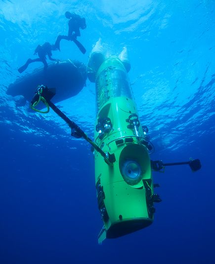 A glowing green torpedo-like capsule underwater with divers