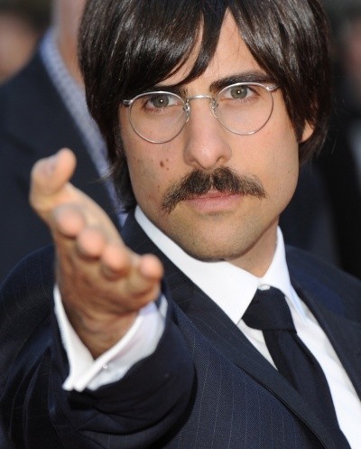 Photo of Jason Schwartzman in glasses, reaching out in a funny-mock-dramatic way to photographers