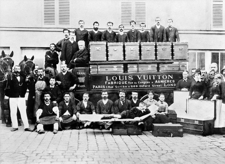 A crowd of employees poses with various Louis Vuitton trunks and bags