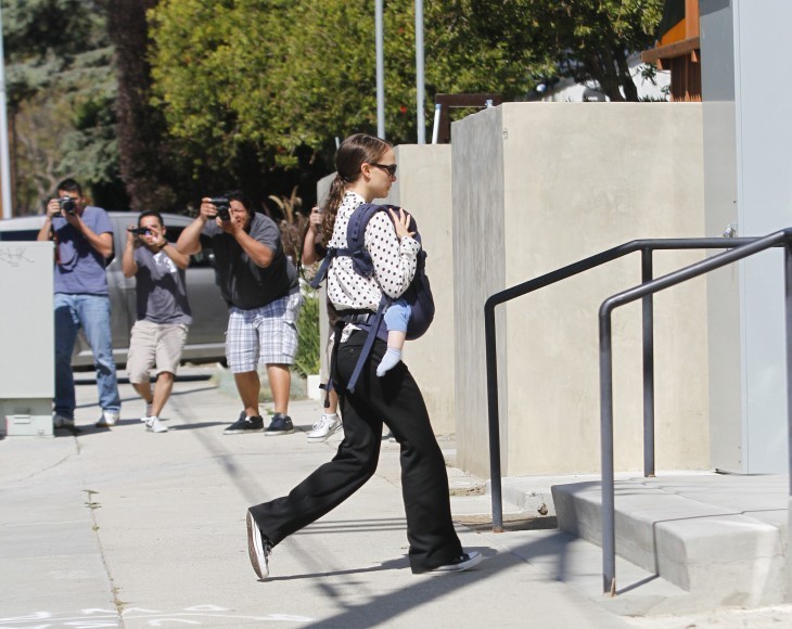Photo of Natalie Portman walking up some steps, baby in a sling, with photographers pointing cameras at her