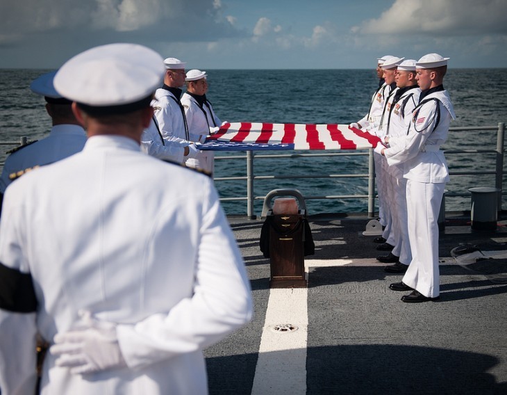 Photo of a ship's deck with sailors holding a flag over Neil Armstrong's urn