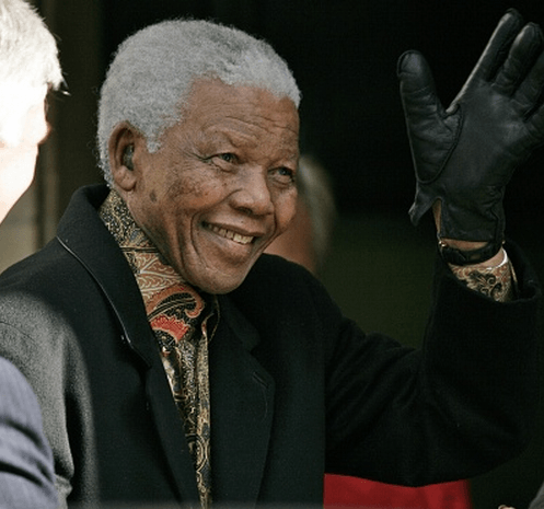 Photo of Nelson Mandela in coat and gloves, smiling and waving