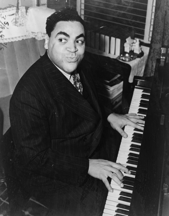 Fats Waller sits with his hands on the piano keys, grinning impishly