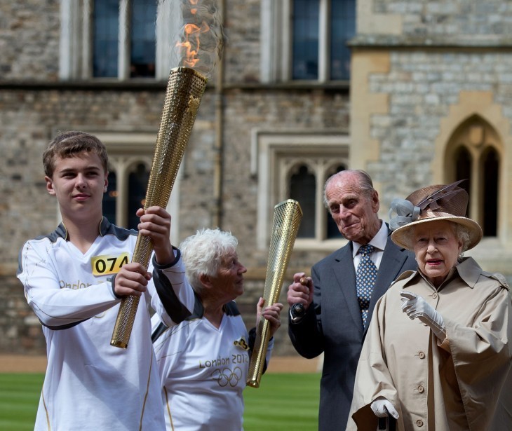 Photo of Queen Elizabeth pointing at a boy holding the Olympic torch as two elders look on