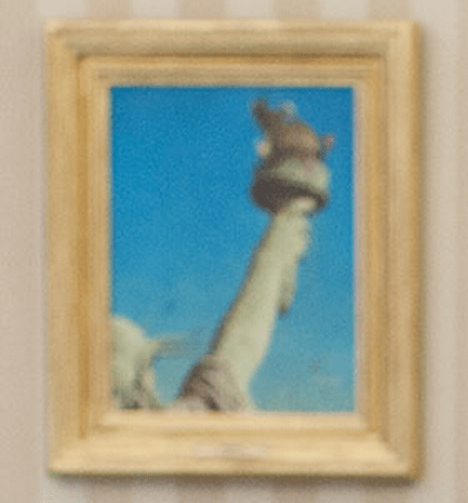 A framed photo of the Statue of Liberty, with just the corner of her head and her outstretched arm and torch showing