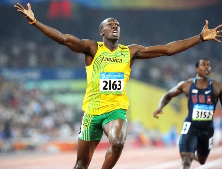 Photo of Usain Bolt raising his hands in triumph as he crosses the finish line in green and yellow running garb