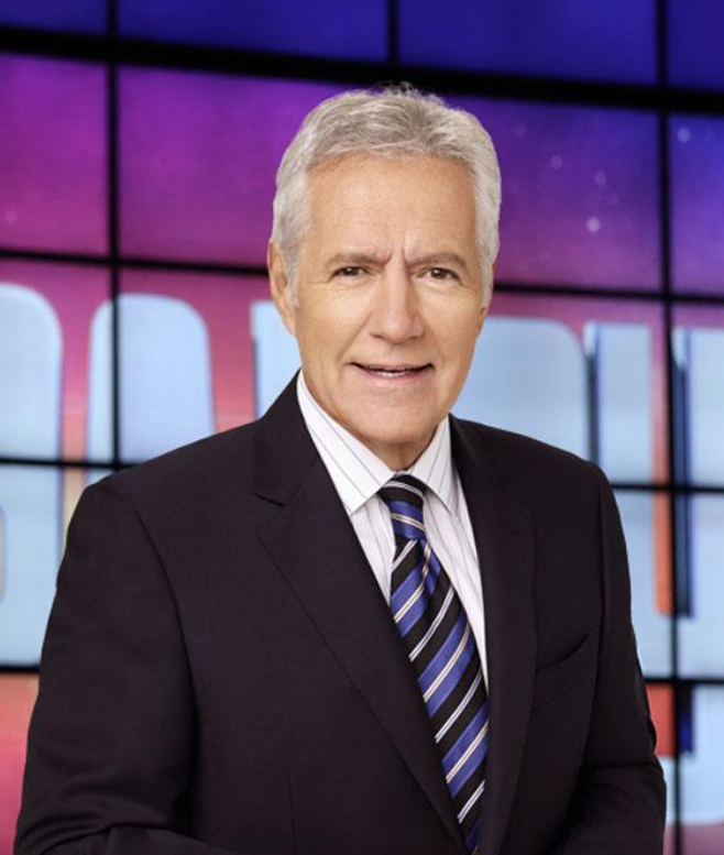 Alex Trebek wears a blue suit and tie, looking good with gray hair on the colorful set of 'Jeopardy!'