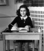 Anne Frank looks up from her school desk and smiles, in a dark dress with a white collar