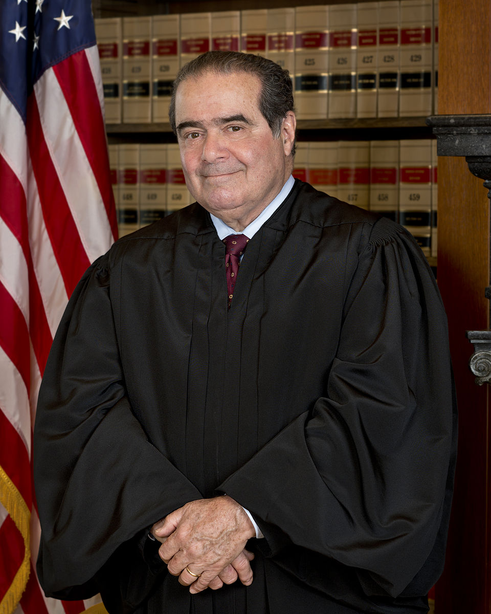 Photo of Antonin Scalia in judicial robes, in front of a flag, smiling at the camera