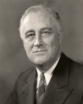 FDR is a gray-haired man in sensible suit with a striped tie. He has a slight smile on his face.