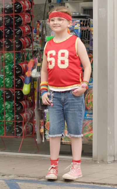 A little girl in thick glasses, a headband and denim shorts, looking nerdy