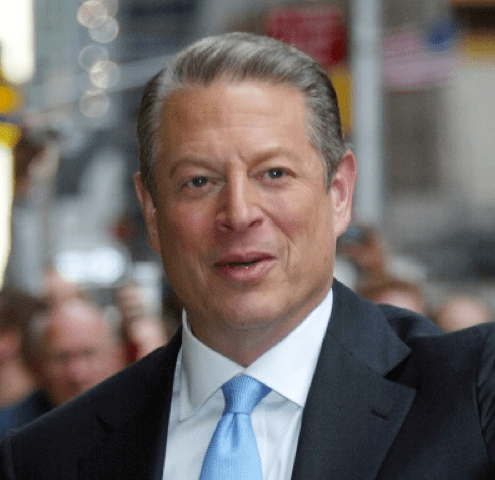 Photo of Al Gore in a blue business suit and silky light blue tie, half smiling as he stands on the street in front of onlookers