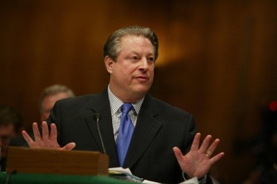 Al Gore stands onstage in a blue tie, talking while gesturing with his hands