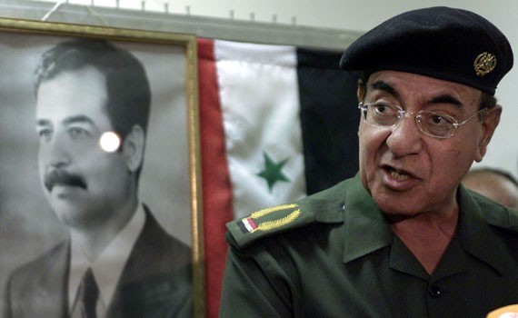 A photo of Baghdad Bob in military uniform, speaking in front of a portrait of Saddam Hussein