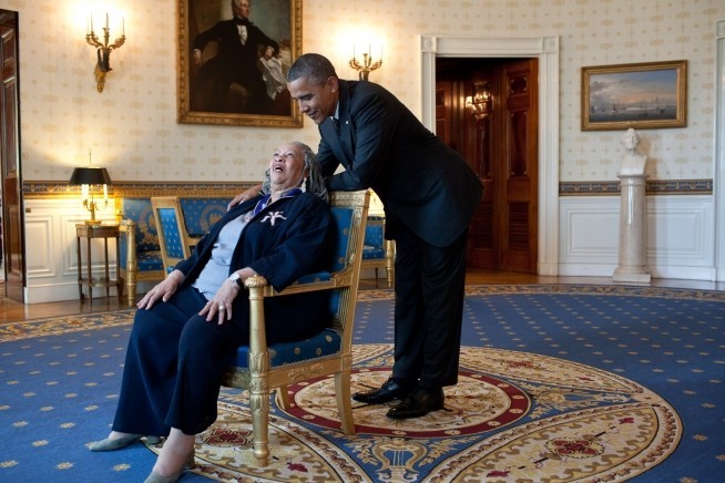 Photo of Barack Obama leaning over the armchair of Toni Morrison as the two share a laugh