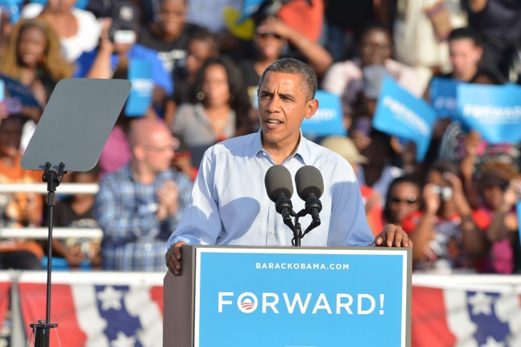 Photo of Barack Obama speaking at a podium with a poster reading 'Forward!'