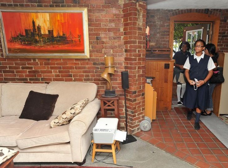 Photo of students walking into an apartment with a tile floor, beige carpet, and a comfy well-worn look