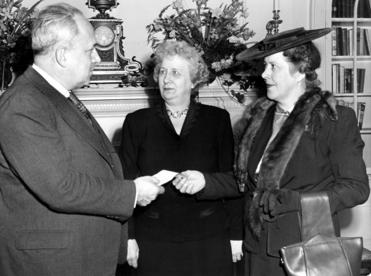 Photo of Bess Truman looking askance between a man in a suit and a woman with a mink stole