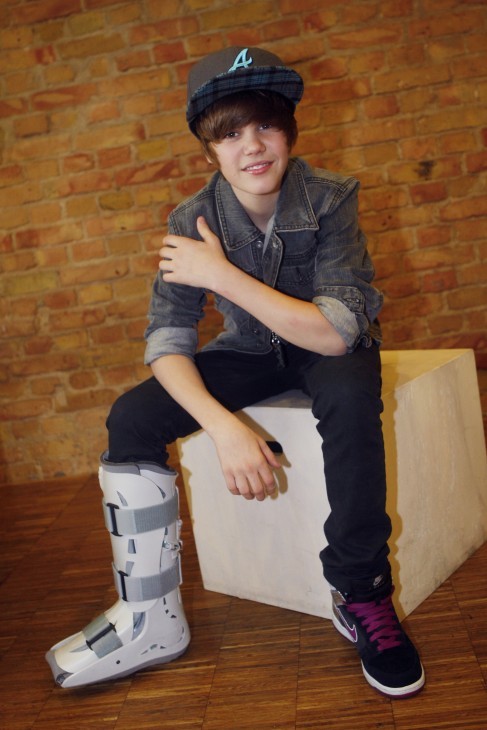 Photo of Justin Bieber sitting with a broken leg in a walking boot and a cap with an 