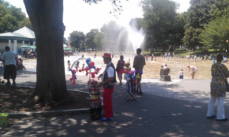 Photo of the Frog Pond at Boston Common, with kids playing in a fountain and a balloon animal maker in foreground