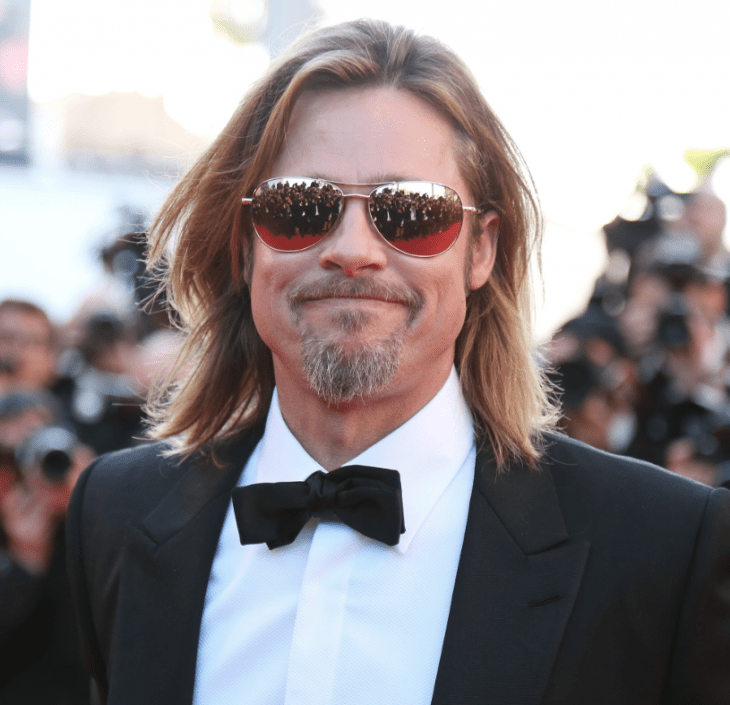 Photo of Brad Pitt smiling on a red carpet, with press photographers reflected in his mirror sunglasses
