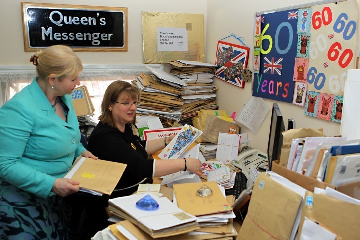 Photo of two women talking as they look over bundles and stacks of mail, with corgi drawings on the wall next to them