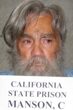 Photo of Charles Manson, in wild gray beard and big hair, with a swastika carved in his forehead