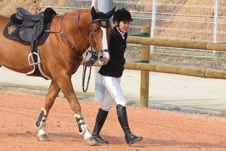 Photo of Charlotte Casiraghi in full equestrian outfit, smiling as she walks her horse