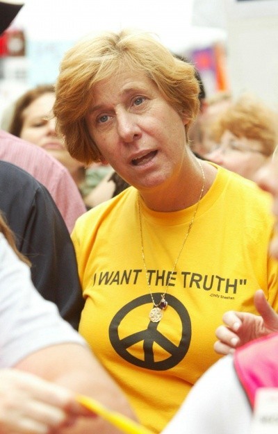 A photo of Cindy Sheehan in a yellow t-shirt reading 'I want the truth' with a peace symbol