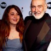 An old balding (and smiling) man poses with a cheerful teenage girl