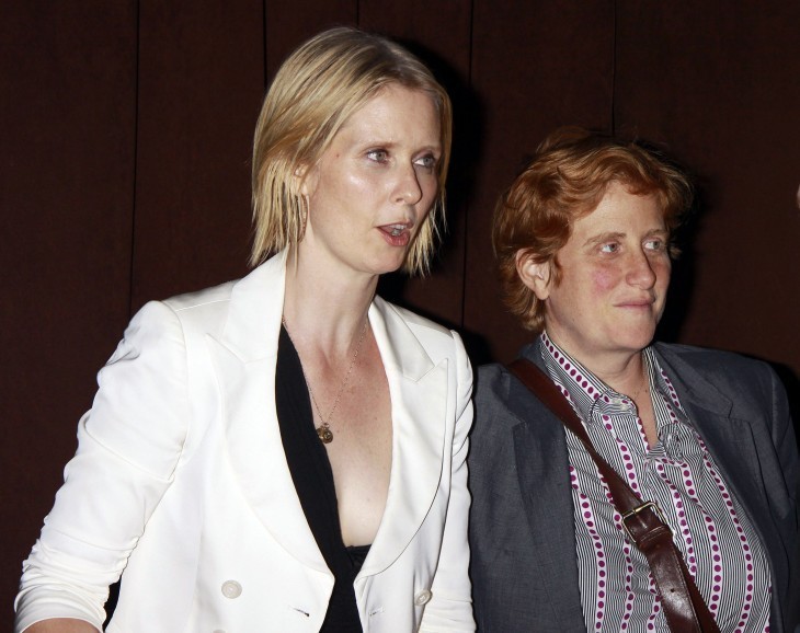 Photo of Cynthia Nixon and her girlfriend, Christine Marinoni, in casual clothes smiling on the street at night