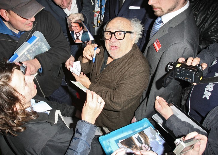 Photo of Danny DeVito smiling as he signs autographs in the midst of an excited clutch of fans