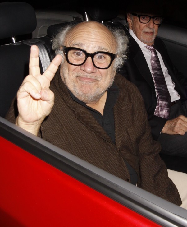 Photo of Danny DeVito flashing a peace sign through the back window of a London lorry, er, automobile. A red one.