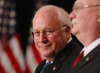 A photo of Dick Cheney, grimace-smiling on a podium in front of an American flag