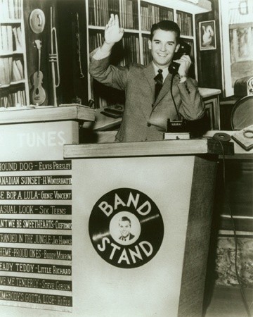 An old black-and-white photo of Dick Clark, very young, grinning behind an American Bandstand podium