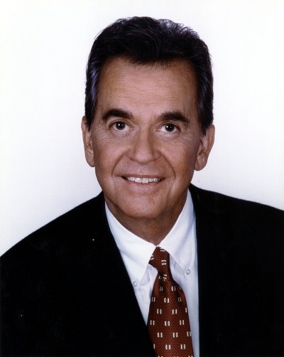 A head shot photo of Dick Clark, in blue suit and red tie, looking older but still dark-haired