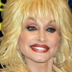 Photo of Dolly Parton in hoop earrings and a big ol' head of platinum blonde hair, smiling. We can just see the top of her gold jacket