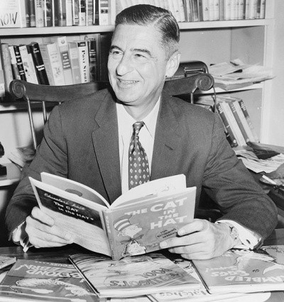 An old photo of Dr. Seuss holding a book and smiling at someone off-camera