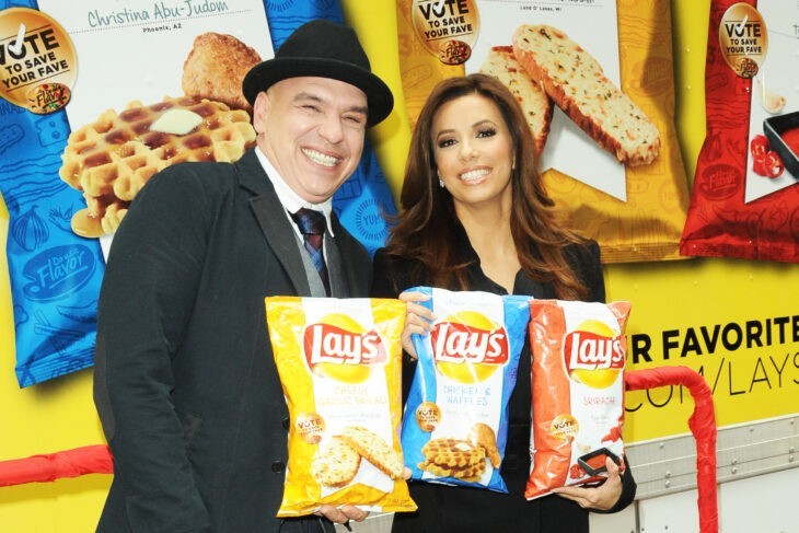 Photo of Eva Longoria plus a guy in a porkpie hat, holding up bags of chips and smiling like mad