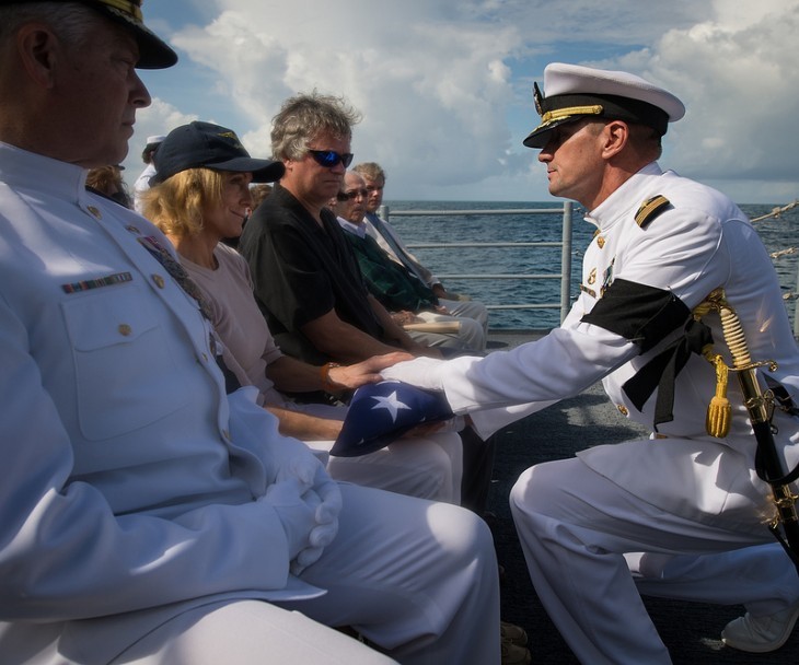 A Navy officer knees as he presents a folded flag to Neil Armstrong's wife