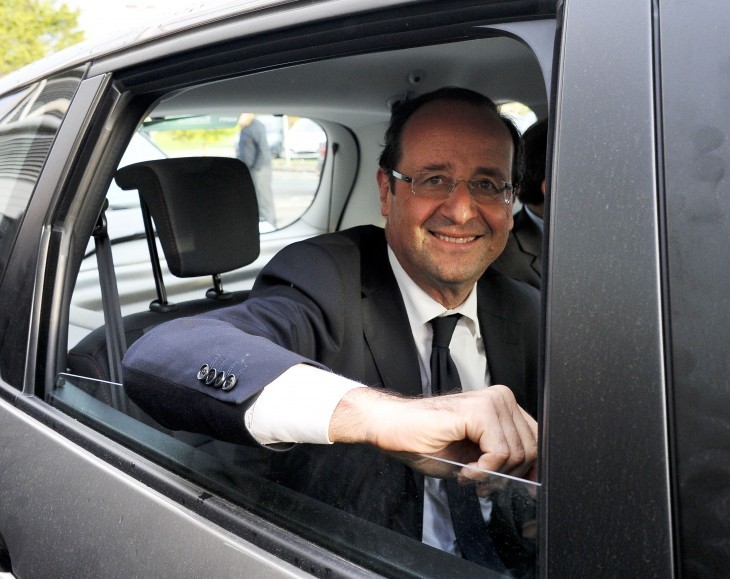 A photo of Francois Hollande, smiling as he leans out the window of his black limousine