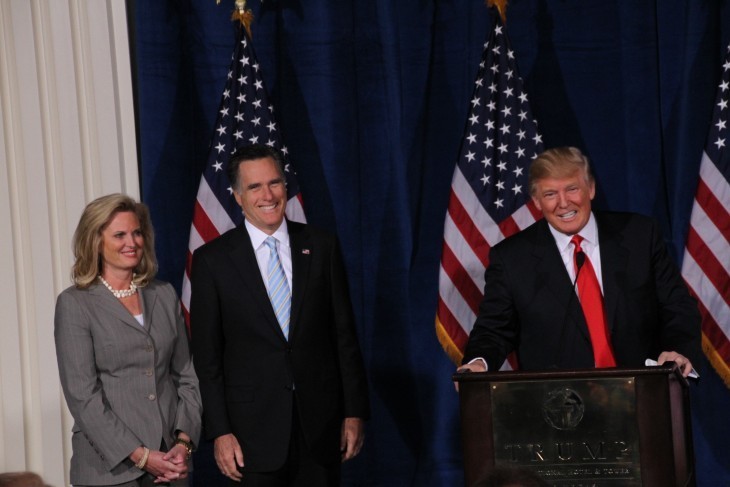 Donald Trump smiles at a podium as Mitt Romney and wife look on