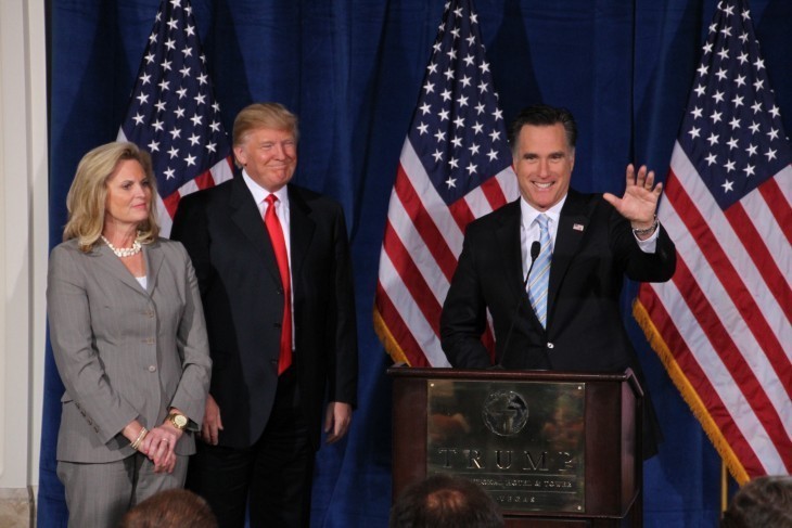 Mitt Romney smiles and waves from podium as Donald Trump looks on