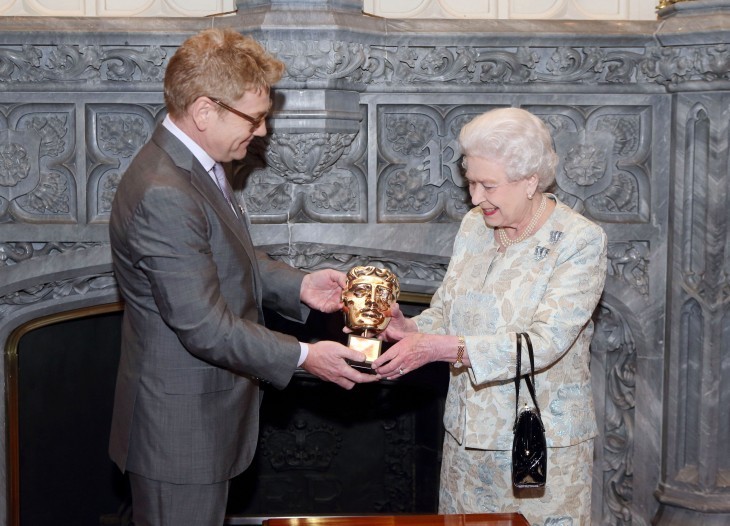 Kenneth Brannagh hands Queen Elizabeth a BAFTA statue: a gold mask/face thingy
